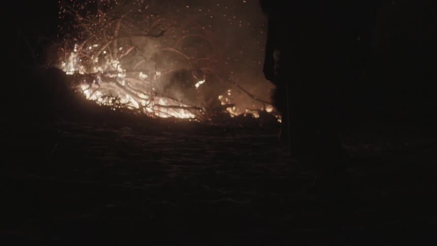 A man approaching a pile of burning brush at night