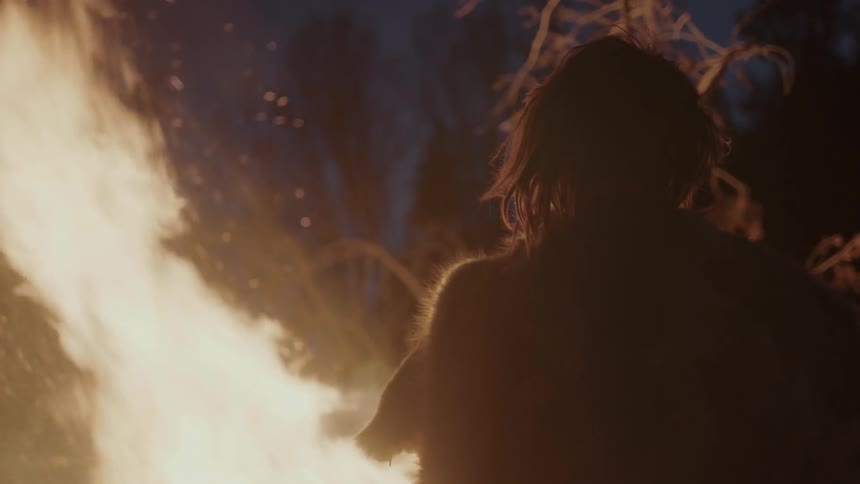 A large bonfire throws flames flames as a person watches it