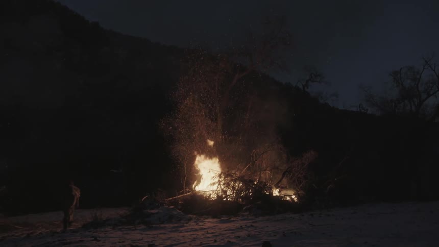 A person walking away from a large bonfire burning at night