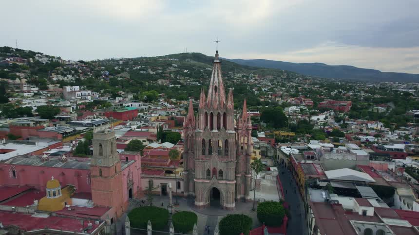 The parroquia de san miguel arcngel church with green hills and neighborhood homes under a cloudy sky