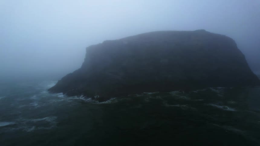 Waves hitting an island on a foggy morning