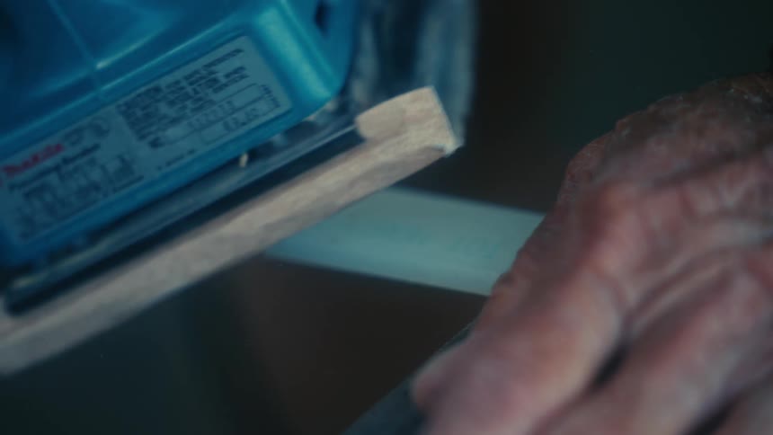 Elderly man uses a small power tool to sand the blade of a knife in the backyard