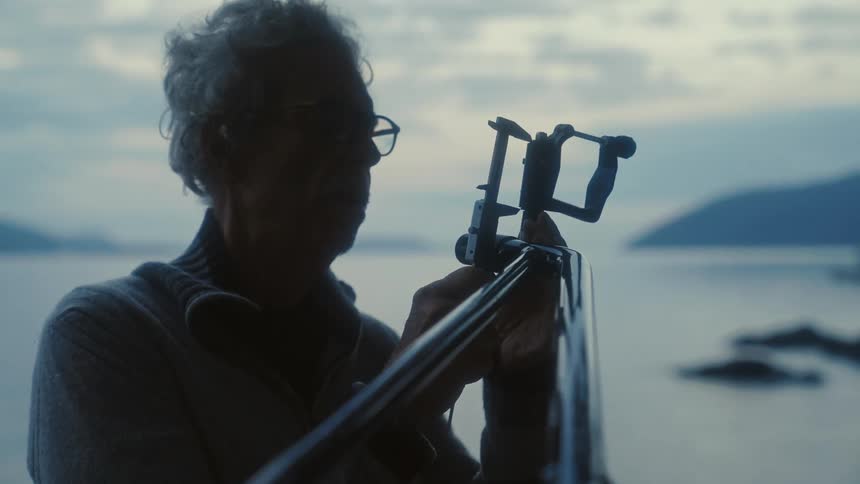 Silhouette of an elderly man carefully measuring a metal structure on the coast of a lake