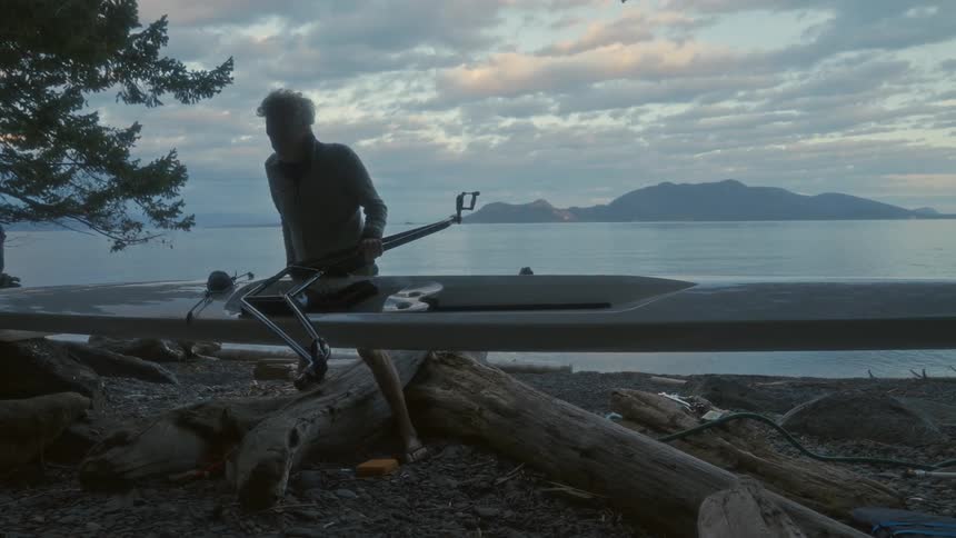 Elderly man assembling a kayak on the coast of a lake next to the ocean at morning