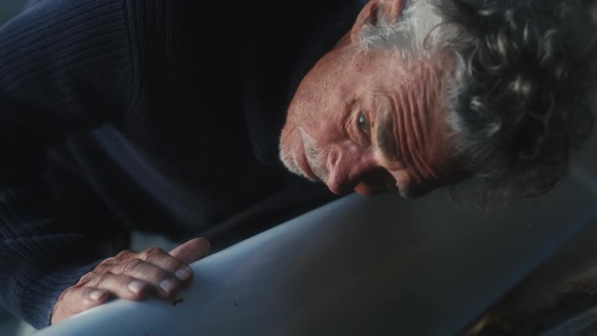 A man looking down the line of a smooth piece of wood lifts his head