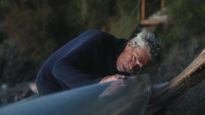 An elderly man runs his hand on the bottom of a kayak