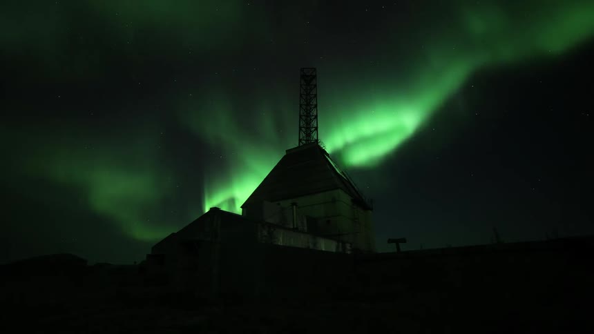 Time lapse of green polar lights aurora borealis shining above the silhouette of a building in the countryside
