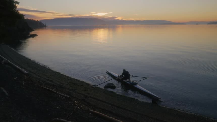 Man gets on sea kayak at sunset