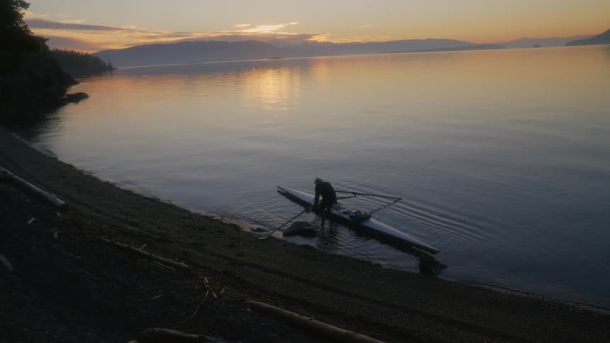 A person climbing out of a kayak on a lake at sunset