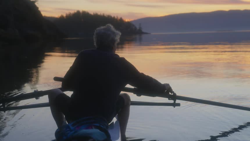 An elderly person sits in a kayak on the shore
