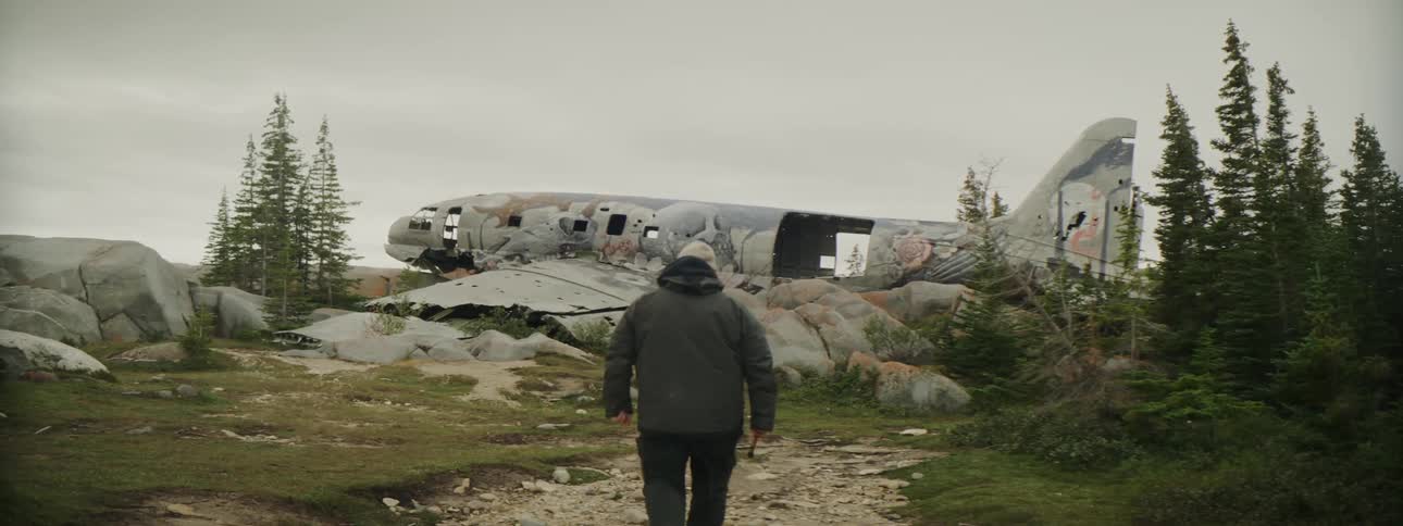 Man walking towards an abandoned airplane at the top of a mountain