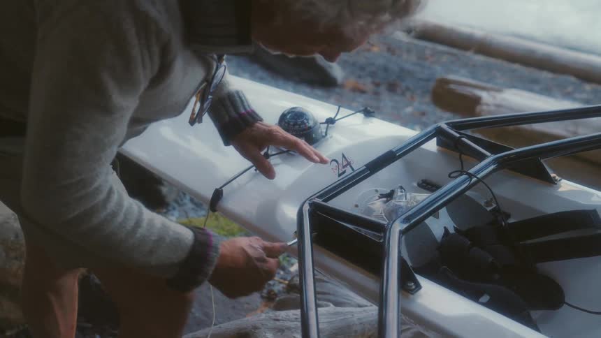 A man repairing a kayak next to a lake