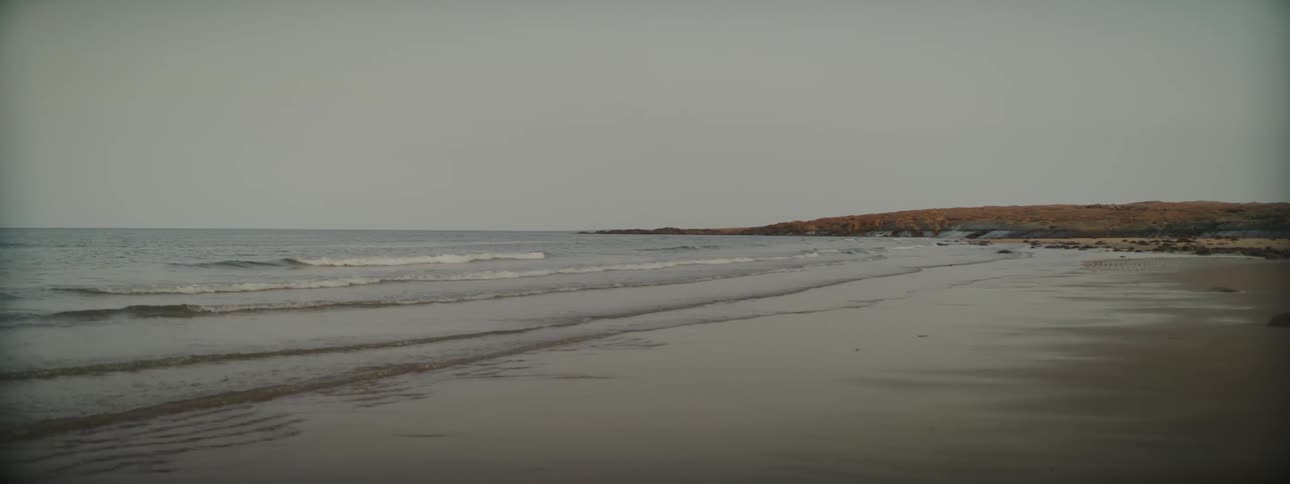 Ocean waves wash into a sandy beach under a cloudy daytime sky
