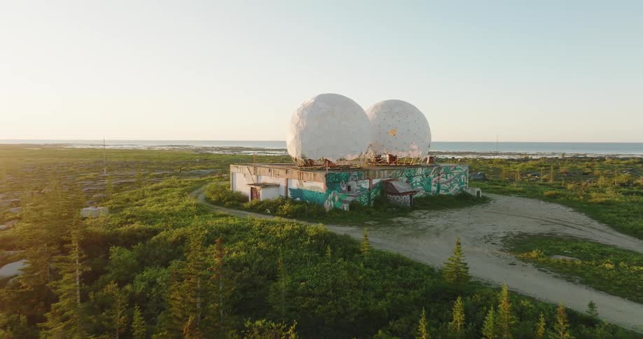 A giant factory topped with large domes sits under construction in an open field
