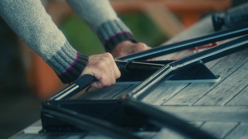 Close up of the hands of an elderly man wearing a sweater fastening metal bars over a wooden table