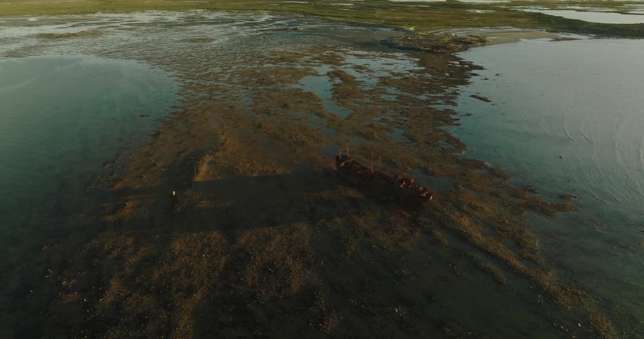 Aerial view of a rusted shipwreck on the surface of a marsh at evening