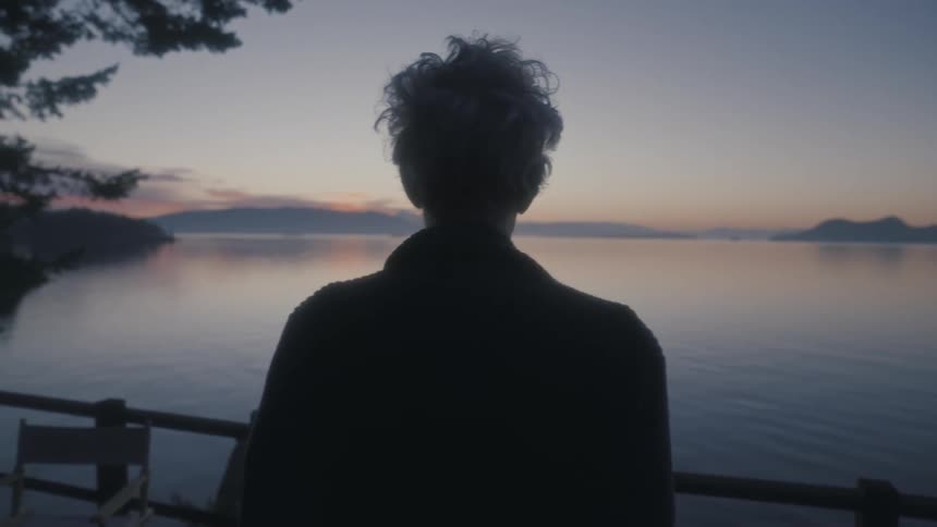 An elderly person stands on the shore and looks out at the ocean