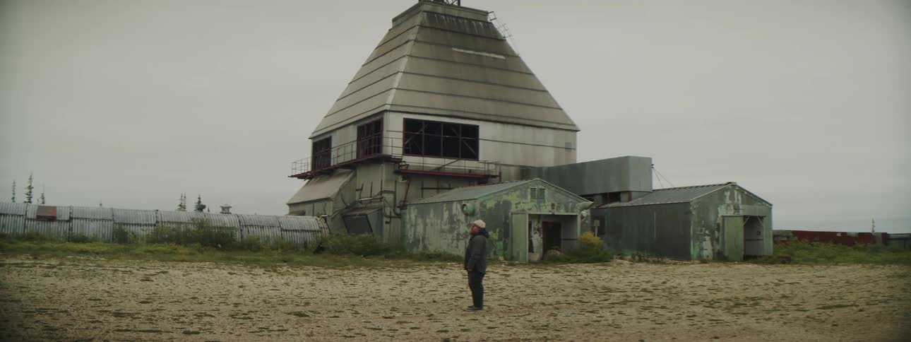 Bearded man standing in front of an abandoned building in the countryside at daytime