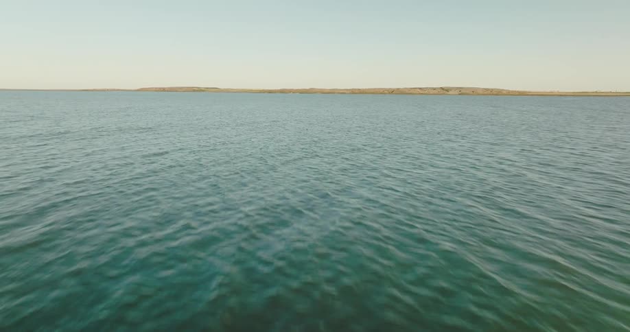 Water ripples and waves under a clear sky as land is on the horizon