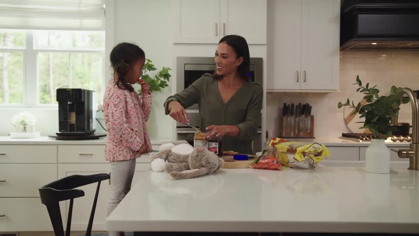 A woman makes her daughter a peanut butter and jelly sandwich in the kitchen