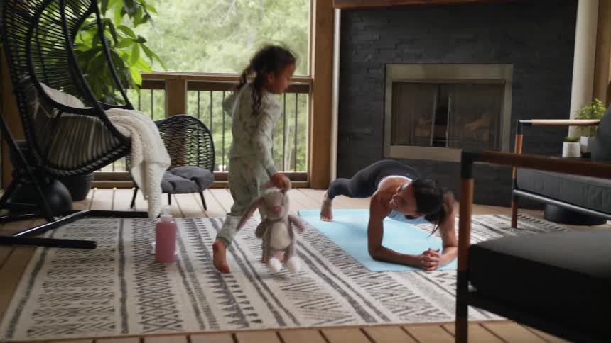 A young girl with a stuffed bunny running towards her mom doing yoga