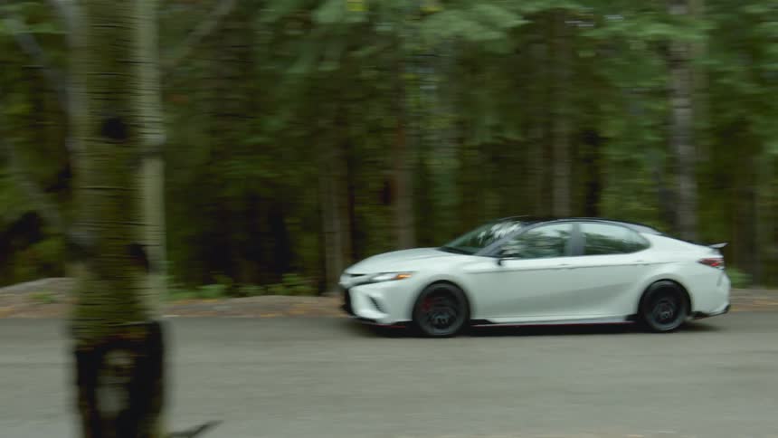 A car travels along a road through woodland during the day