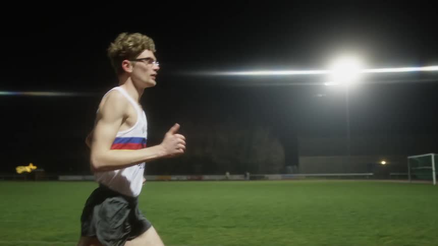 A man runs along a running track on a athletics field at night