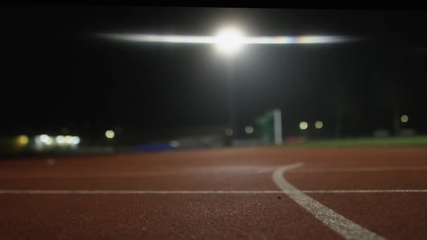 An athlete is standing on the field and then he runs as a light shines brightly in the distance