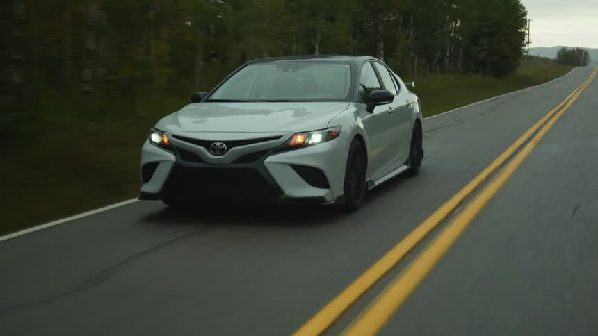 A vehicle drives down a rural highway past a forest
