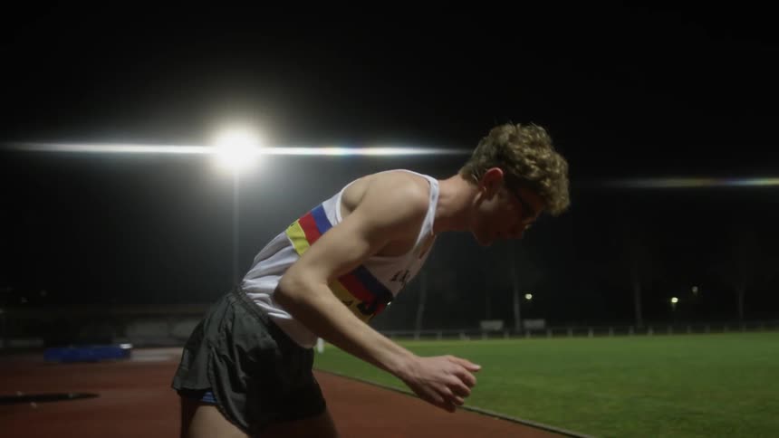 A track runner is standing on the field as he gets on his mark and is ready to run