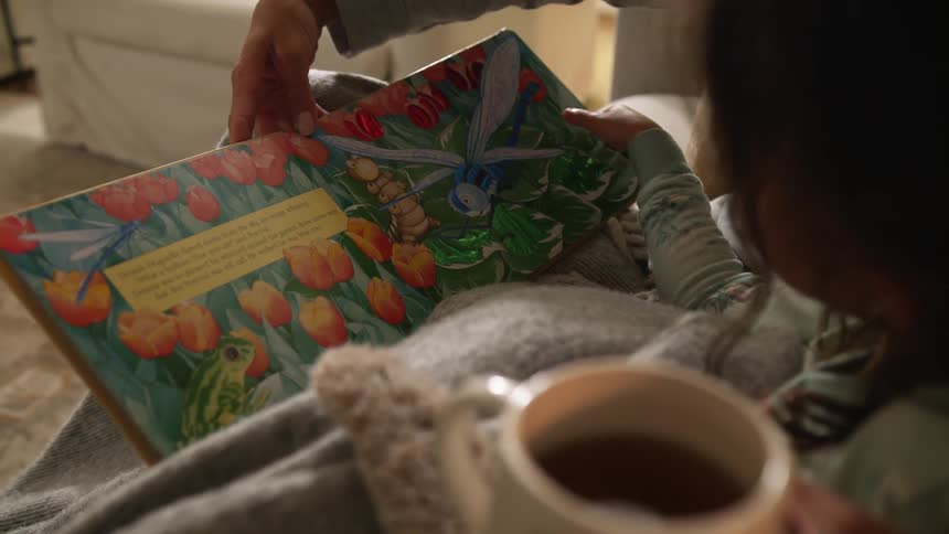 Mother holding a cup of tea reading a storybook on the couch at home