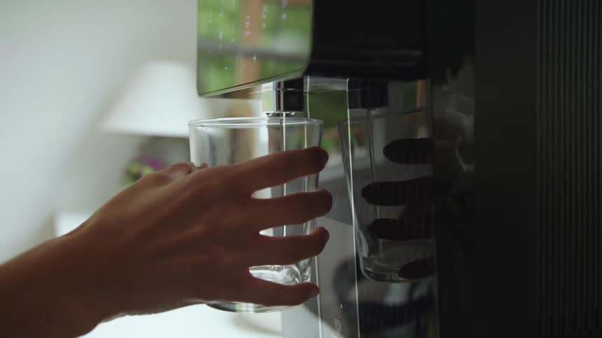 Close up of the hand of a woman filling a glass on a modern water filter at home