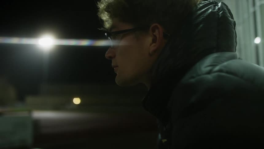 Side profile of man wearing glasses and black coat lifting his head up at night