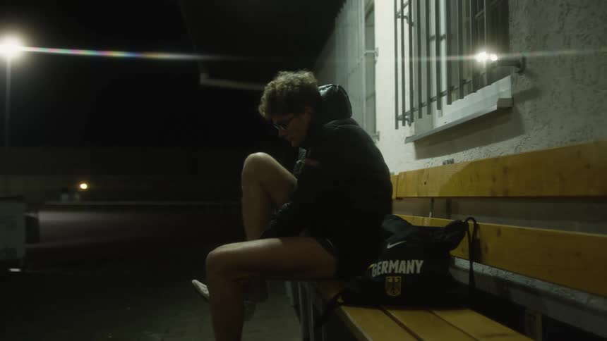 A man puts on running shoes while sitting on a bench outside