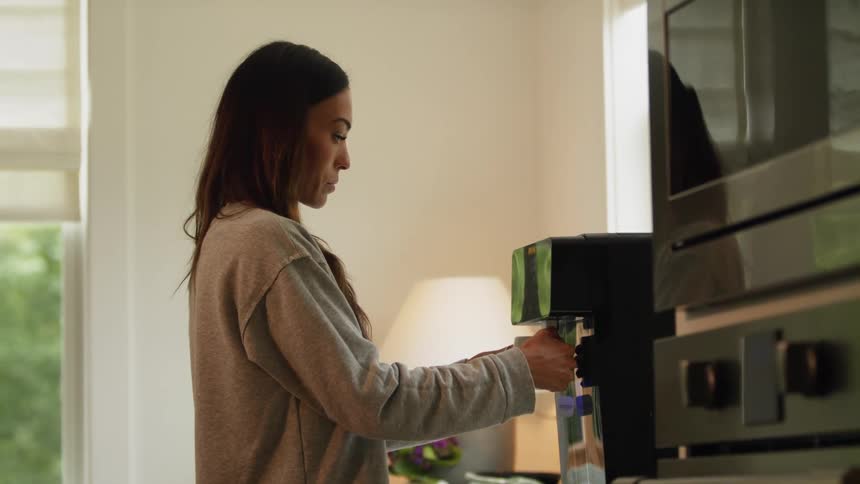 Woman with brown hair and gray sweatshirt makes coffee with coffee machine in the kitchen