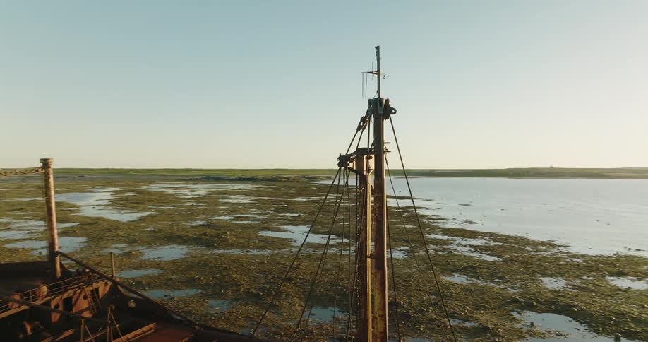 Sun shine reflects off water in distance while shipwreck sits on shore