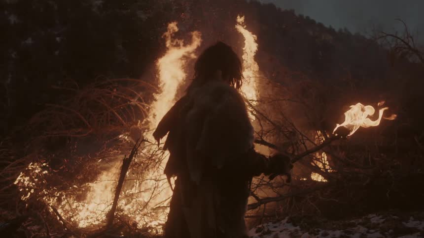 Man with torch stands beside a burning brush pile