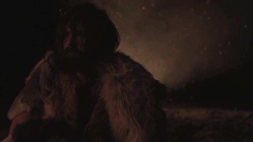 Man dressed in furs has his back to a large fire
