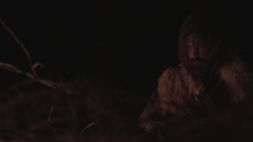 Wilderness man sitting in the dark next to a fire