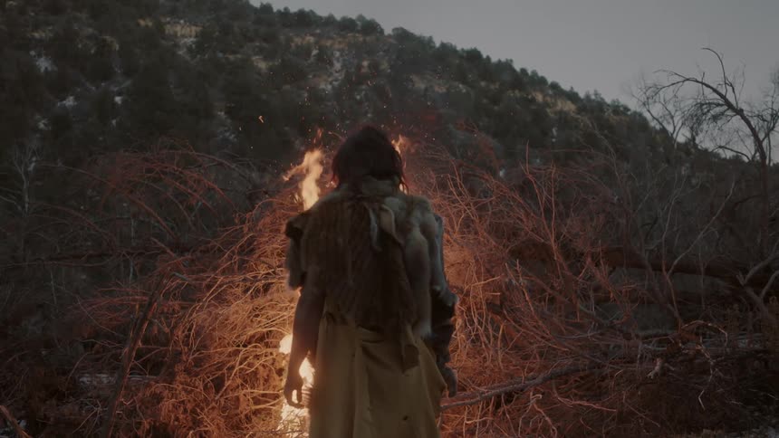 A man stands with back to the viewer watching a large bonfire go up in flames