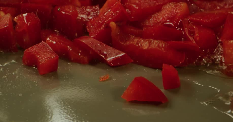 Close up of red sliced peppers being fried in frying pan