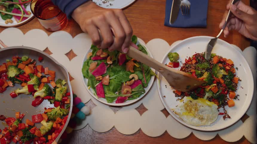 A woman spoons stir fried vegetables onto a plate