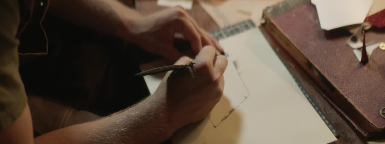 A man uses a quill pen to draw a line in notebook