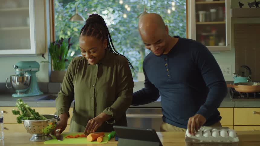 A man and woman smile at one another while preparing food together in a home kitchen