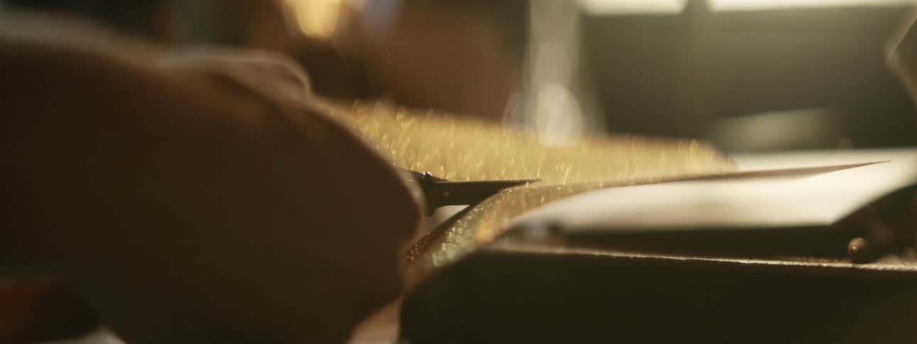 Hands using small sharp scissors to cut a strip of gold glitter covered paper