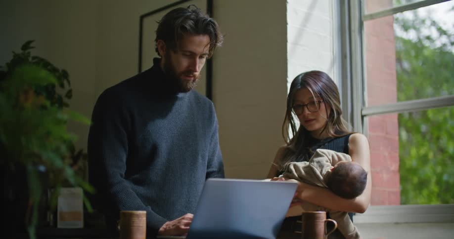 Woman holds baby as she and man discuss contents on laptop