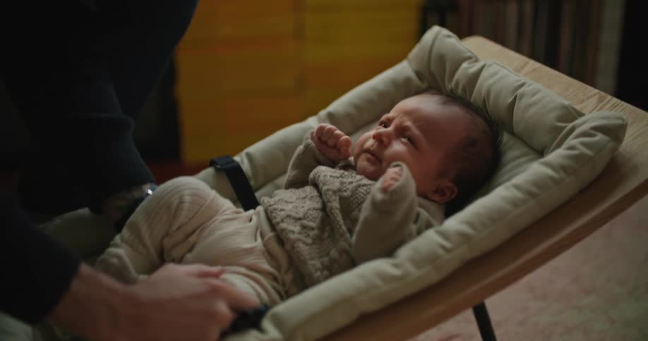 Father places baby in modern infant rocker and straps the child securely