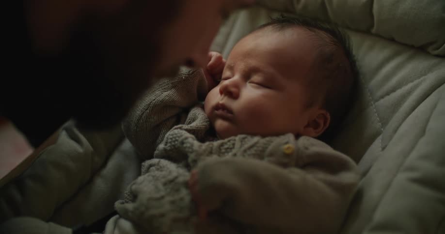 Bearded young man cuddles and talks to his newborn baby at home