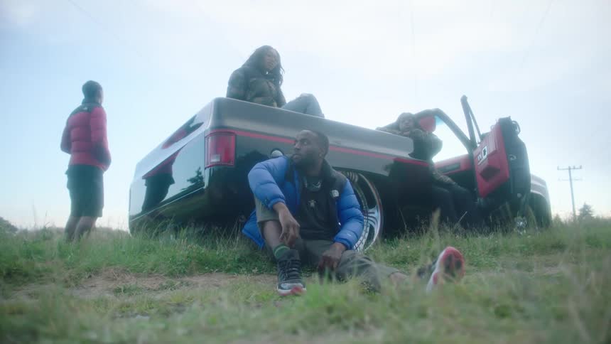 Group of models wearing thick jackets sitting on and around a parked convertible car in the countryside