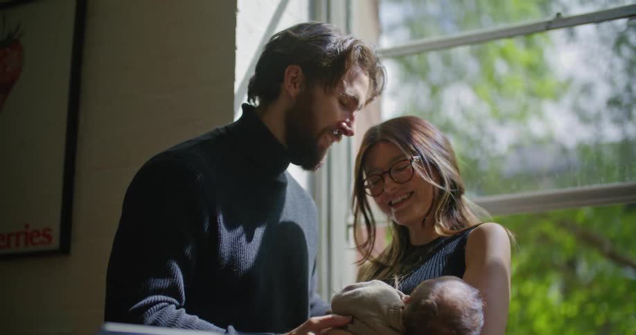 Parents lean against each other and smile at their baby